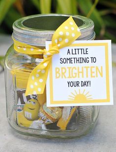 a jar filled with yellow and white candies next to a sign that says, a little something to brighten your day