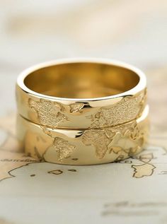 two gold wedding bands with the world map on them, sitting on top of a map