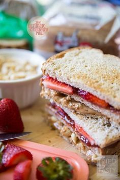 a cut in half sandwich sitting on top of a cutting board next to strawberries