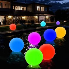 glowing balls are floating in the water at night near a large house and lawn area