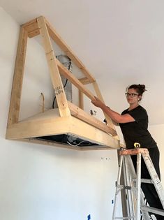 a woman standing on a ladder working on a bed frame