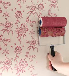 a person using a roller to paint a wall with pink flowers and vines on it