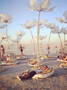 many people are sitting in the sand with sculptures made out of plastic bottles and flowers