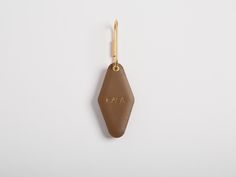 a brown leather keychain hanging from a hook on a white wall with the word aa in gold lettering