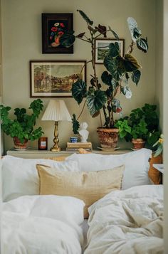 a bed with white linens and potted plants on the headboard in front of it