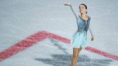 a female figure skating on the ice in a short skirt and blue top with her arms outstretched