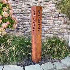 a wooden pole with numbers on it in front of a brick wall and flower garden