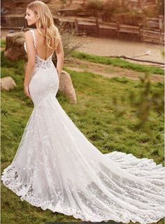 a woman in a wedding dress is standing on the grass with her back to the camera