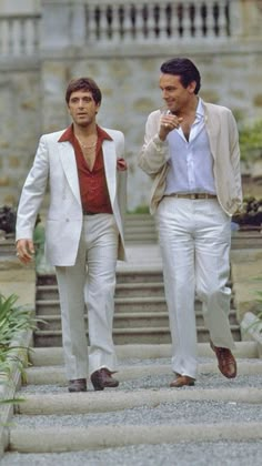 two men in white suits walking down some steps and one is holding his hand up to his mouth