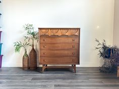 a wooden dresser sitting next to two vases on top of a hard wood floor