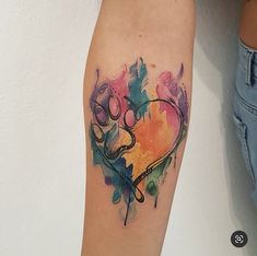 a colorful heart tattoo on the right arm and leg, with watercolor splashs