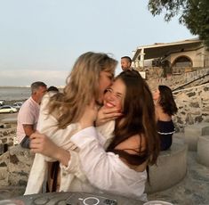 two women are kissing each other on the beach while others look on in the distance