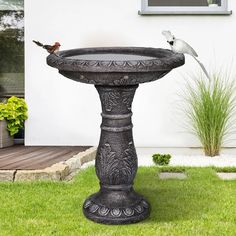 two birds perched on top of a bird bath in the grass next to a house