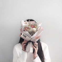 a woman holding a bouquet of flowers in front of her face while wearing a white shirt