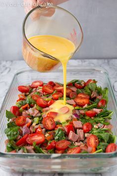 someone is pouring dressing into a salad in a glass dish with tomatoes and lettuce