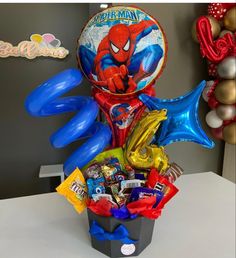 a spiderman balloon in a basket filled with candy, balloons and confetti