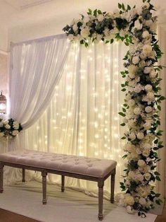 a wedding ceremony setup with white flowers and greenery on the wall, along with a bench