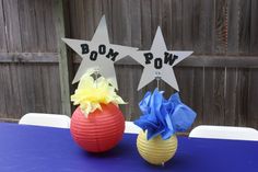 two paper balls with bows are sitting on a blue tablecloth and one is decorated with stars that say boom pow