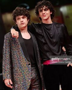 two men standing next to each other on a red carpet