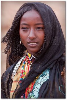 a woman with braids wearing a scarf and headdress is looking at the camera