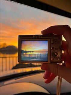 a person holding up a small camera with a sunset in the back ground behind them