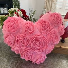 a heart - shaped arrangement of pink roses sits on a table in front of a fireplace