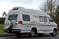 an rv is parked on the side of the road in front of some grass and trees