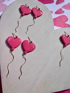 three pink heart shaped earrings are hanging from hooks on a white surface with hearts in the background