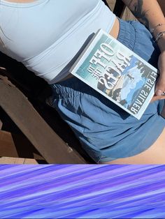 a woman sitting on a bench holding a book in her lap and looking at the camera