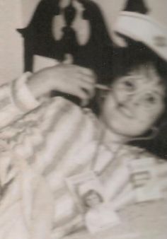 an old black and white photo of a boy in bed with a hat on his head