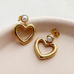 "Bold, feminine studs adorned with a faux pearl bezel and dropped hearts. Dress 'em up or keep 'em casual paired alongside your favorite sweater.  Hearts measures 17mm. 1\" drop with a 6mm bezel.  Our materials make for an amazing, high quality, seamless, jewelry piece with longevity. Our earrings are plated with 18k gold, 18k rose gold, or rhodium and finished with a protective coating. A little secret we'll keep between us: it looks way more than it costs." Trendy Heart Earrings For Mother's Day, Hearts Dress, Silver Statement Earrings, Gold Statement Earrings, Between Us, Statement Drop Earrings, Bow Earrings, Favorite Sweater, Accessories Jewelry Earrings