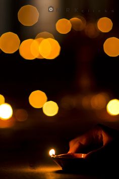 a person holding a lit candle in their hand on a table with blurry lights behind them