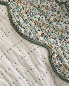 an unmade quilted blanket laying on top of a white bed sheet with green trim