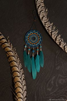 a blue dream catcher hanging from a wall next to feathers on a black tablecloth