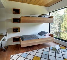 a bedroom with two bunk beds and a desk in front of a window that looks out onto the woods