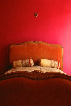 a bed in a room with red walls and pillows on the headboard, next to a window