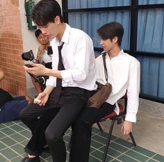 two young men sitting next to each other while looking at their cell phones in front of them