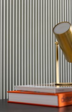 a gold desk lamp sitting on top of a stack of books next to a white wall