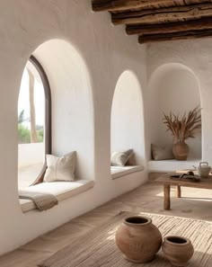 a living room with white walls and arched windows on the wall is filled with potted plants