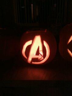 two pumpkins carved to look like avengers logos, one with the letter a on it