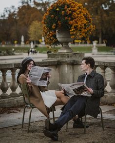 a man and woman are sitting on chairs reading the paper in front of a fountain