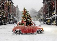 a small red car with a christmas tree on top in the middle of a snowy street