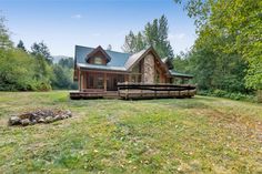 a log cabin sits in the middle of a grassy area with trees and grass around it