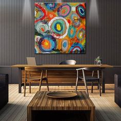 an abstract painting hangs on the wall above a wooden table