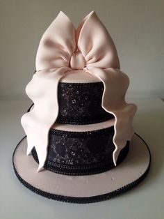 a three tiered cake with a pink bow on top and black lace around the edges