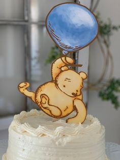 a white cake with a blue balloon on top and a brown teddy bear figurine