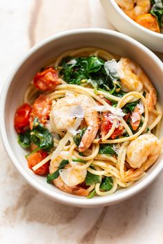 two bowls of pasta with shrimp, spinach and tomatoes on a marble countertop