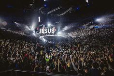 a large group of people standing in front of a stage with jesus on the screen