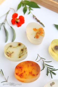 four different types of soap sitting on top of a white surface next to flowers and leaves