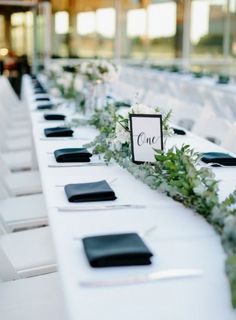 the table is set up with black and white place cards, greenery, and silverware